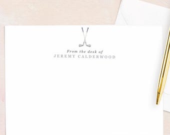 May include: A stationery set featuring a white card with the text "From the desk of Jeremy Calderwood" and a golf club graphic. A gold pen and a white envelope are also present. The background is a light pink and beige.