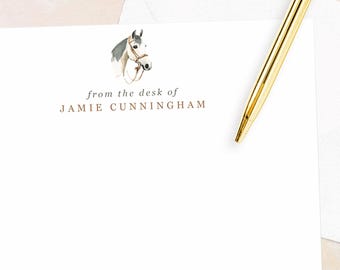 May include: White stationery set featuring a watercolor horse illustration and gold text that reads "from the desk of Jamie Cunningham." A gold pen rests on the stationery, with a white envelope in the background.