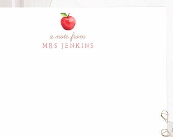 May include: A white rectangular stationery card featuring a small watercolor red apple illustration at the top center. Below the apple, the text reads a note from MRS JENKINS in a simple font. A matching white envelope is positioned behind the card.