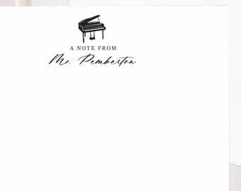 May include: A white stationery card and matching envelope. The card features a small black illustration of a grand piano centered at the top, followed by the printed text A NOTE FROM and the personalized name Mr. Pemberton in black ink.