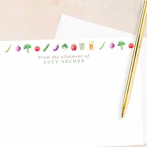 May include: A white stationery set with a watercolour vegetable border. The text "From the allotment of LUCY ARCHER" is printed on the stationery. A gold pen rests on the stationery, with a white envelope.