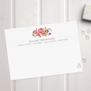 May include: A white card with a floral design and the text "HILARY REYNOLDS" and "2 Green Lane, Ambridge, Berkshire, AM3 3TH".