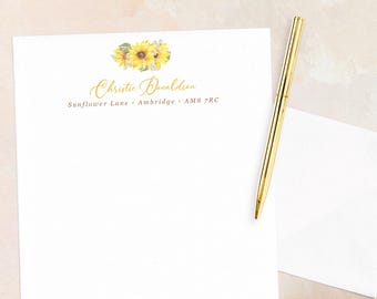 May include: White stationery with a sunflower design and gold script text. The text reads "Christie Donaldson" and an address. A gold pen rests on the stationery and a white envelope.