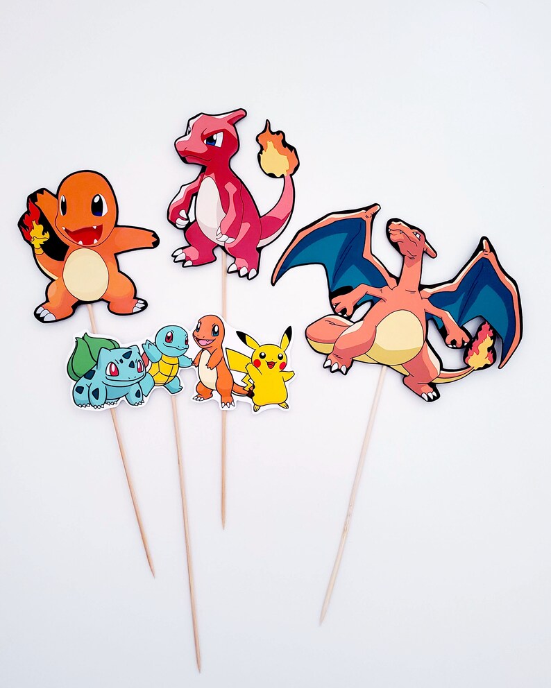 May include: Set of six Pokemon character cake toppers. The toppers feature Pikachu, Charmander, Squirtle, Bulbasaur, Charizard, and Dragonite. The characters are printed on cardstock and attached to wooden skewers.