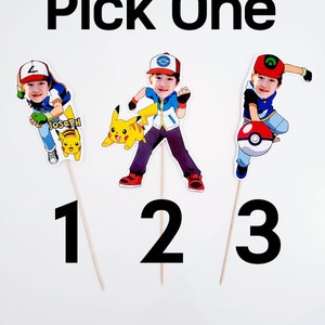 May include: Three printable cupcake toppers featuring a cartoon character dressed as a Pokemon trainer. The character has a different pose and accessory in each topper. The first topper features a Pikachu, the second topper features a Pokeball, and the third topper features a Pokeball with a green symbol. The text "Pick One" is at the top of the image.