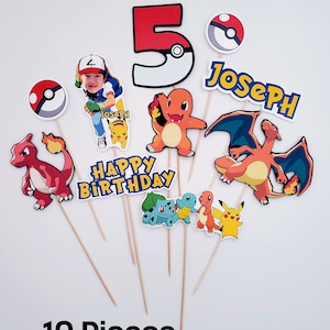 May include: Ten colorful Pokemon themed cake toppers with a red number 5, a character with a photo, a red and orange Pokemon, a blue and orange Pokemon, a yellow Pokemon, a green and brown Pokemon, a red and orange Pokemon, a red and orange Pokemon, a blue and yellow name banner that says "Joseph", and a yellow banner that says "Happy Birthday".