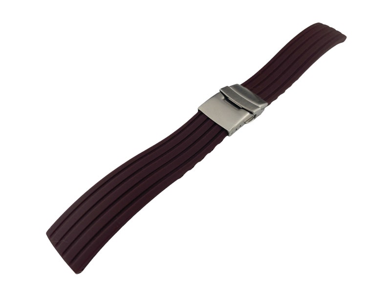 Puede incluir: Una correa de reloj de silicona marr&oacute;n oscuro con una hebilla plateada. La correa tiene una textura acanalada.