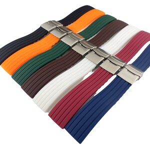 May include: A set of eight watch bands in various colors, including black, orange, green, brown, white, red, and blue. The bands are made of silicone and have a ribbed texture. Each band has a silver buckle.