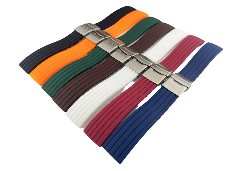 May include: A set of eight watch bands in various colors, including black, orange, green, brown, white, red, and blue. The bands are made of silicone and have a ribbed texture. Each band has a silver buckle.