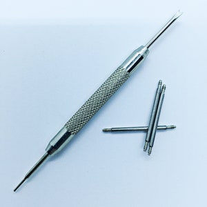 Peut inclure: Un outil de bracelet de montre argent&eacute; avec une extr&eacute;mit&eacute; pointue et une extr&eacute;mit&eacute; fourchue. Il y a quatre broches de bracelet de montre argent&eacute;es &agrave; c&ocirc;t&eacute; de l'outil.