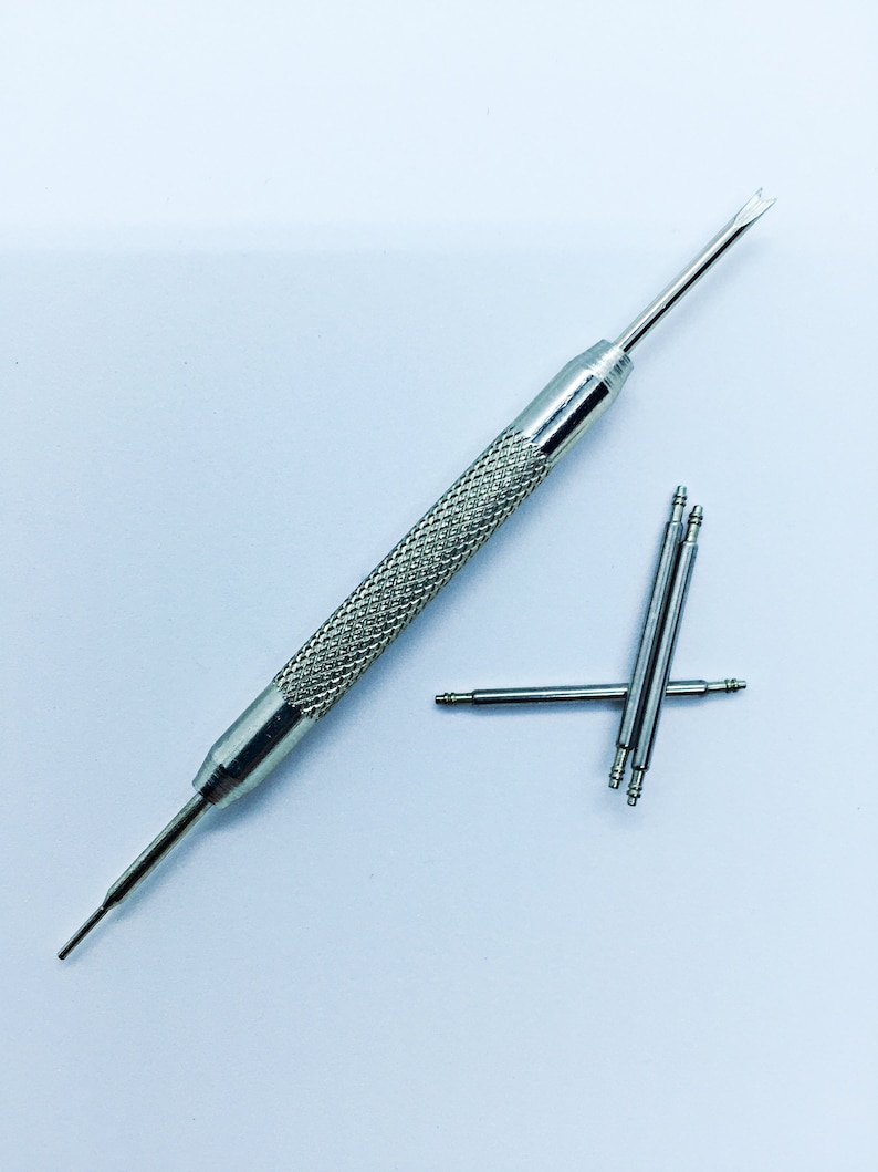 Peut inclure: Un outil de bracelet de montre argent&eacute; avec une extr&eacute;mit&eacute; pointue et une extr&eacute;mit&eacute; fourchue. Il y a quatre broches de bracelet de montre argent&eacute;es &agrave; c&ocirc;t&eacute; de l'outil.