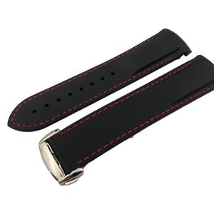 May include: Black watch strap with red stitching. The strap is made of a smooth, flexible material and features a stainless steel buckle. The strap is designed to fit a watch.