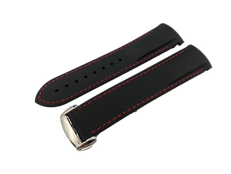 May include: Black watch strap with red stitching. The strap is made of a smooth, flexible material and features a stainless steel buckle. The strap is designed to fit a watch.