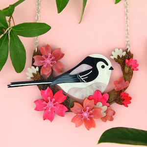 Peut inclure: Un pendentif en résine et métal représentant un mésange à longue queue noir et blanc perché sur une branche avec des fleurs de cerisier roses.