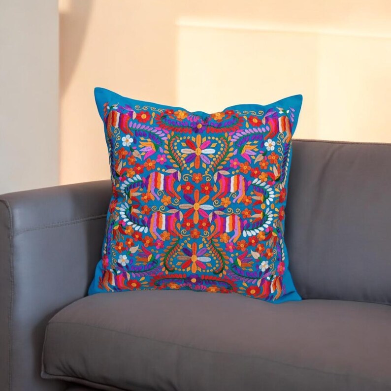 May include: A blue throw pillow with a colorful floral embroidery design. The embroidery features a variety of flowers, leaves, and vines in shades of pink, orange, yellow, green, and purple.
