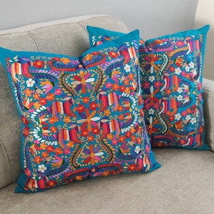 May include: Two turquoise blue throw pillows with colorful embroidered floral patterns. The pillows are on a gray couch.