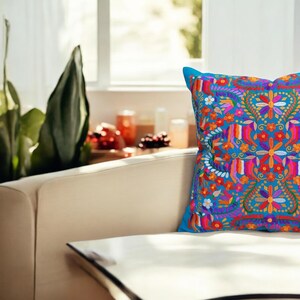 May include: A blue throw pillow with a colorful embroidered floral pattern. The pillow is on a white couch.