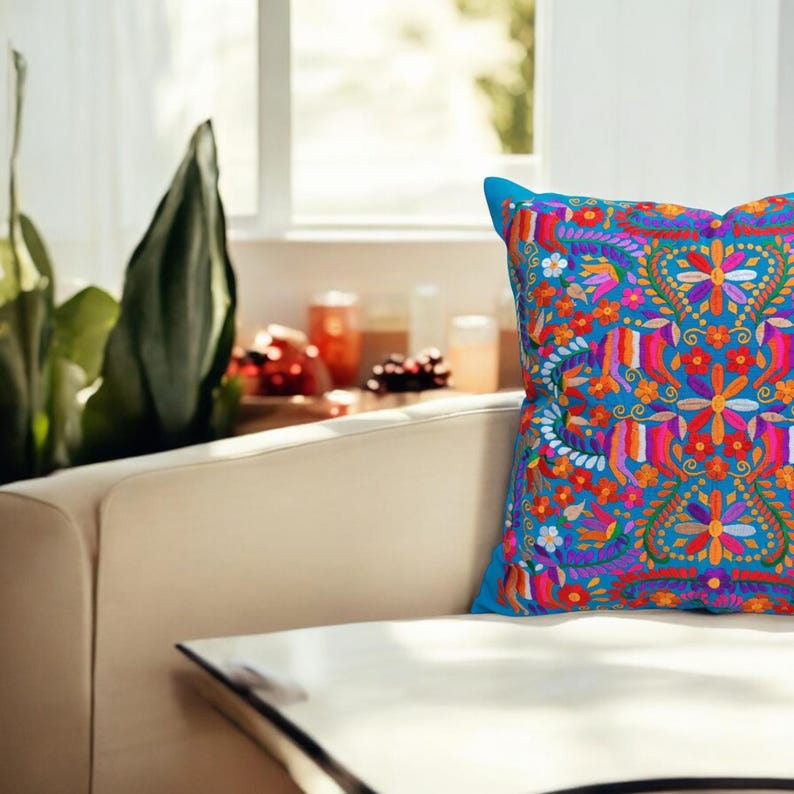 May include: A blue throw pillow with a colorful embroidered floral pattern. The pillow is on a white couch.