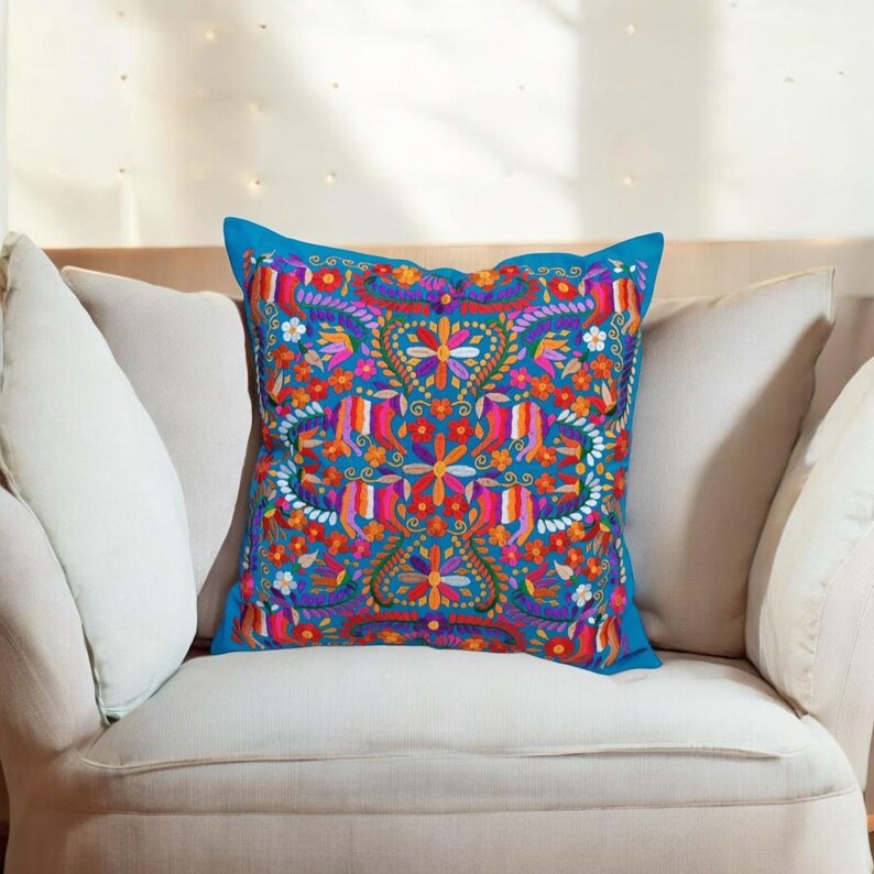 May include: A blue throw pillow with a colorful embroidered floral pattern. The pillow is on a light blue couch.