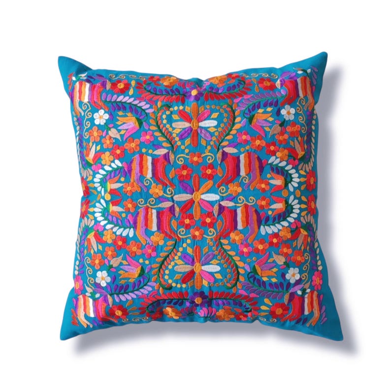 May include: A turquoise blue throw pillow with a colorful floral embroidery design. The embroidery features a variety of flowers in shades of pink, red, orange, yellow, and purple.