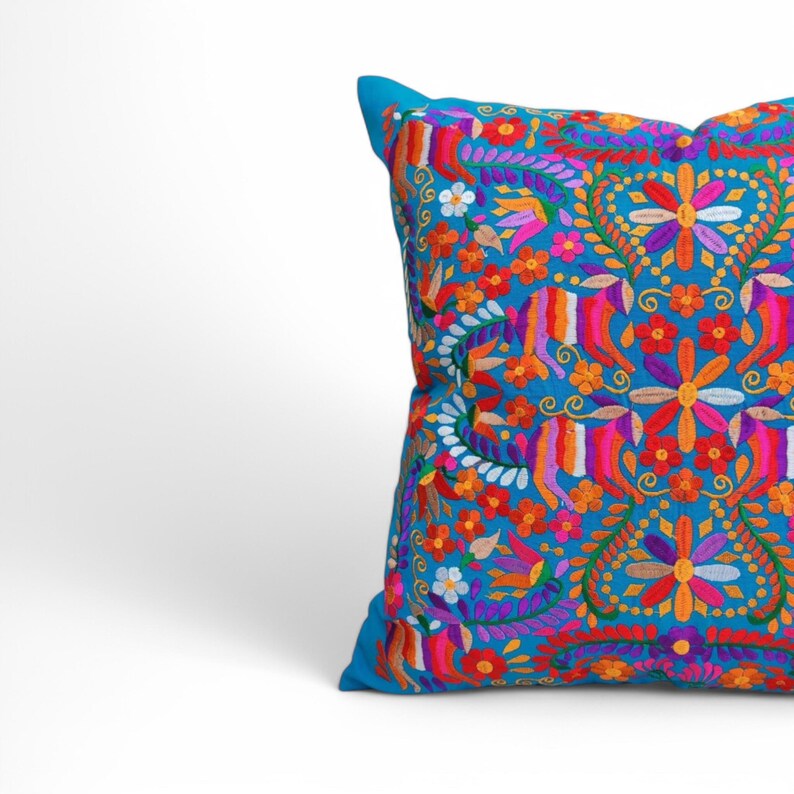 May include: A turquoise blue throw pillow with a colorful embroidered floral pattern. The design features bright pink, orange, red, yellow, and purple flowers and leaves.