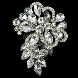 May include: A large silver brooch with a floral design. The brooch is made of clear rhinestones and has a teardrop shape.