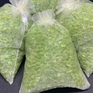 Può includere: Quattro piccole borse di rete bianca riempite con perle di gel verde chiaro. Le borse sono legate con un nastro bianco.