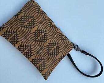 May include: A brown cork clutch with a black geometric pattern and a black wrist strap.