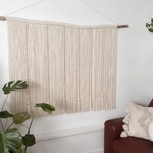 Tapiz o colgante de pared en color crema neutro con detalles de cuentas y borlas de madera