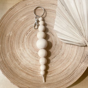May include: A wooden bead keychain with a silver key ring. The keychain is made of natural wood beads and has a simple, minimalist design.