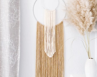 May include: A beige and white macrame wall hanging with two circular hoops. The hanging is made with yarn and beads and has a fringe at the bottom.
