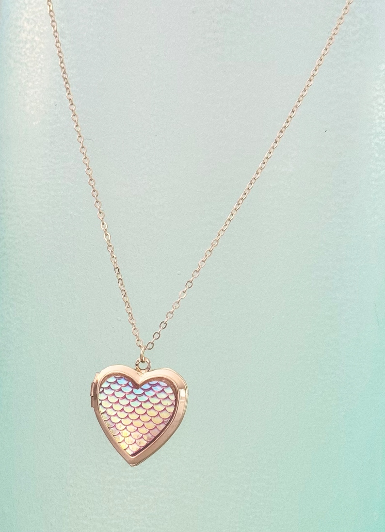 One-of-a-kind gold heart shaped locket with iridescent and pink undertones mermaid/fish scales inlaid on the front! This locket can hold up to 2 photos. It can even be purchased with your photos printed and placed inside by our shop.