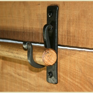 May include: A black metal towel rack with a wooden dowel and a decorative scroll design. The rack is mounted to a wooden wall.