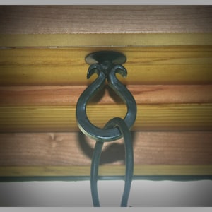 May include: Black metal hook with a decorative design, attached to a wooden ceiling.
