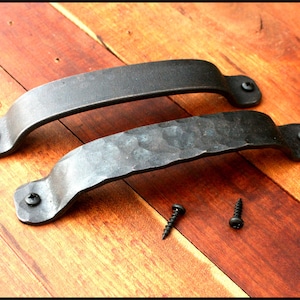 May include: Two black metal door pulls with a hammered finish. The pulls are shown on a wooden surface with two screws.