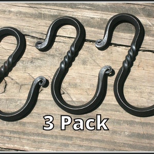 May include: Three black metal S-shaped hooks with a twisted design. The hooks are displayed on a wooden surface. 3 Pack.
