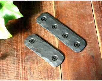 May include: Two black metal rectangular plates with four screw holes each. The plates have a hammered texture and are lying on a wooden surface.