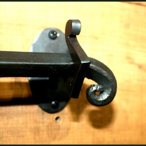 Puede incluir: Barra toallero de metal negro con un diseño decorativo de volutas. La barra está montada en una superficie de madera.