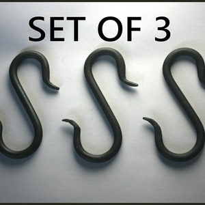May include: Set of three black metal S-shaped hooks. The hooks are approximately 10 cm long and are made of forged steel.