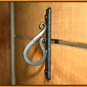 Könnte beinhalten: Ein schwarzer Metallhaken mit einem dekorativen Wirbeldesign ist an einer Holzoberfläche befestigt.