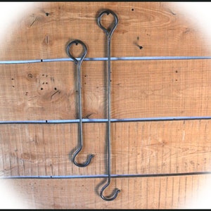 May include: Two black metal hooks hanging on a wooden wall. The hooks are different sizes and have a simple, rounded design.