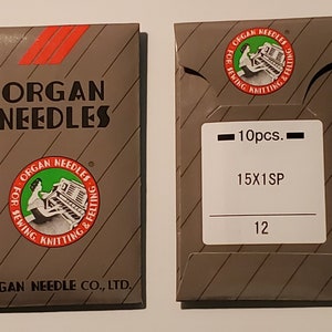 May include: Two grey rectangular paper packets of Organ Needles. The left packet features the brand name, three red diagonal stripes, and a circular logo. The right packet displays the logo, the text 10pcs., 15X1SP, and the number 12.