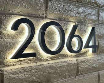 May include: Black illuminated house numbers with a white outline, mounted on a brick wall. The numbers read "2064".