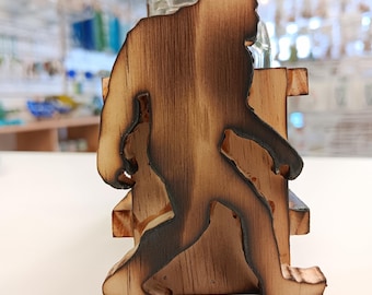 May include: Wooden salt and pepper shaker holder featuring a silhouette of a Bigfoot. The holder is made of natural wood with a dark brown finish.