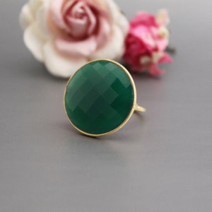 May include: A green gemstone ring with a gold setting. The ring features a large, round, faceted gemstone.