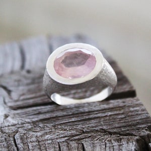 May include: A silver ring with a large, oval-shaped, light pink gemstone set in a bezel setting.