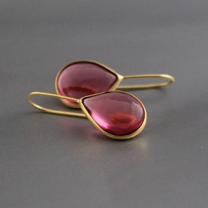 Può includere: Un paio di orecchini pendenti in oro con pietre di vetro rosa a forma di goccia.