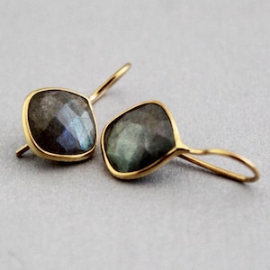 Puede incluir: Un par de pendientes dorados con piedras preciosas cuadradas, iridiscentes, de color gris verdoso. Las piedras están engastadas en un bisel dorado y tienen una superficie facetada. Los pendientes tienen un diseño de gancho simple.
