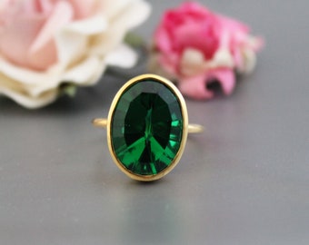 Pode incluir: Um anel de ouro com uma grande gema verde esmeralda de forma oval.