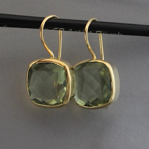 Peut inclure: Une paire de boucles d'oreilles en or avec des pierres précieuses vertes carrées. Les boucles d'oreilles ont un design simple et sont parfaites pour tous les jours.